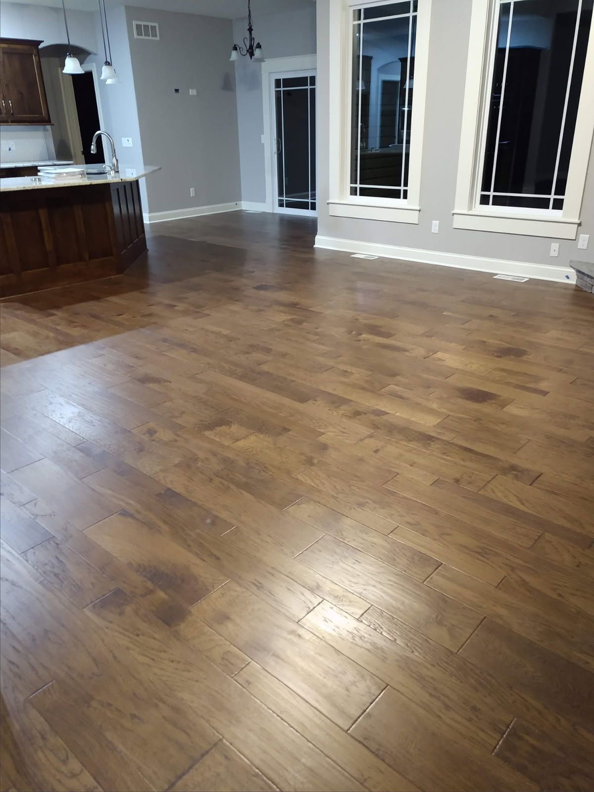 A living room with hardwood floors and a kitchen in the background.