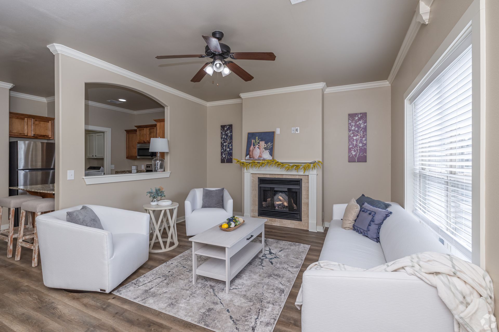 Living room with white furniture, fireplace, and open kitchen view.