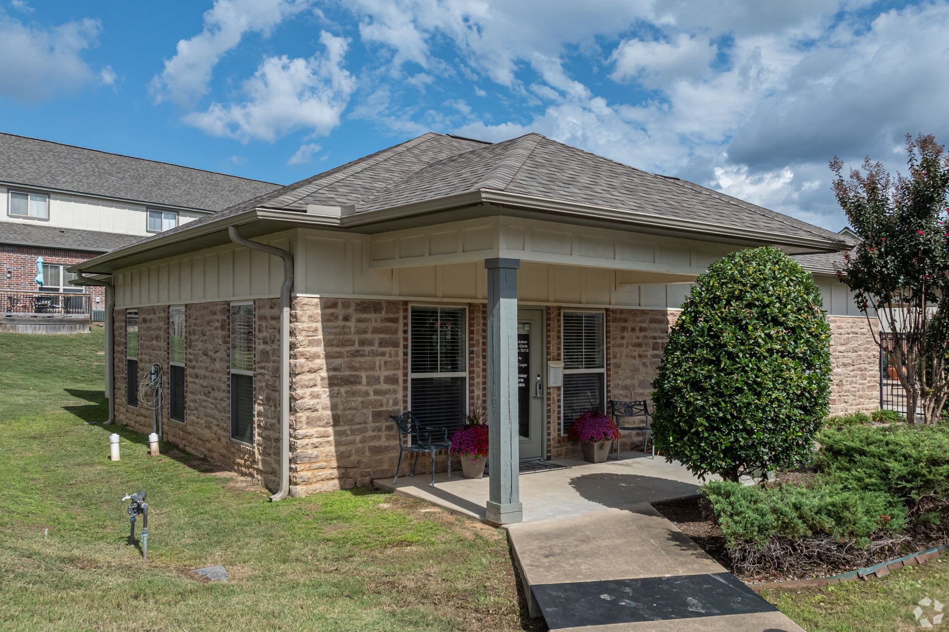 Single-story brick building with a covered entrance, a small front yard, and a cloudy sky.