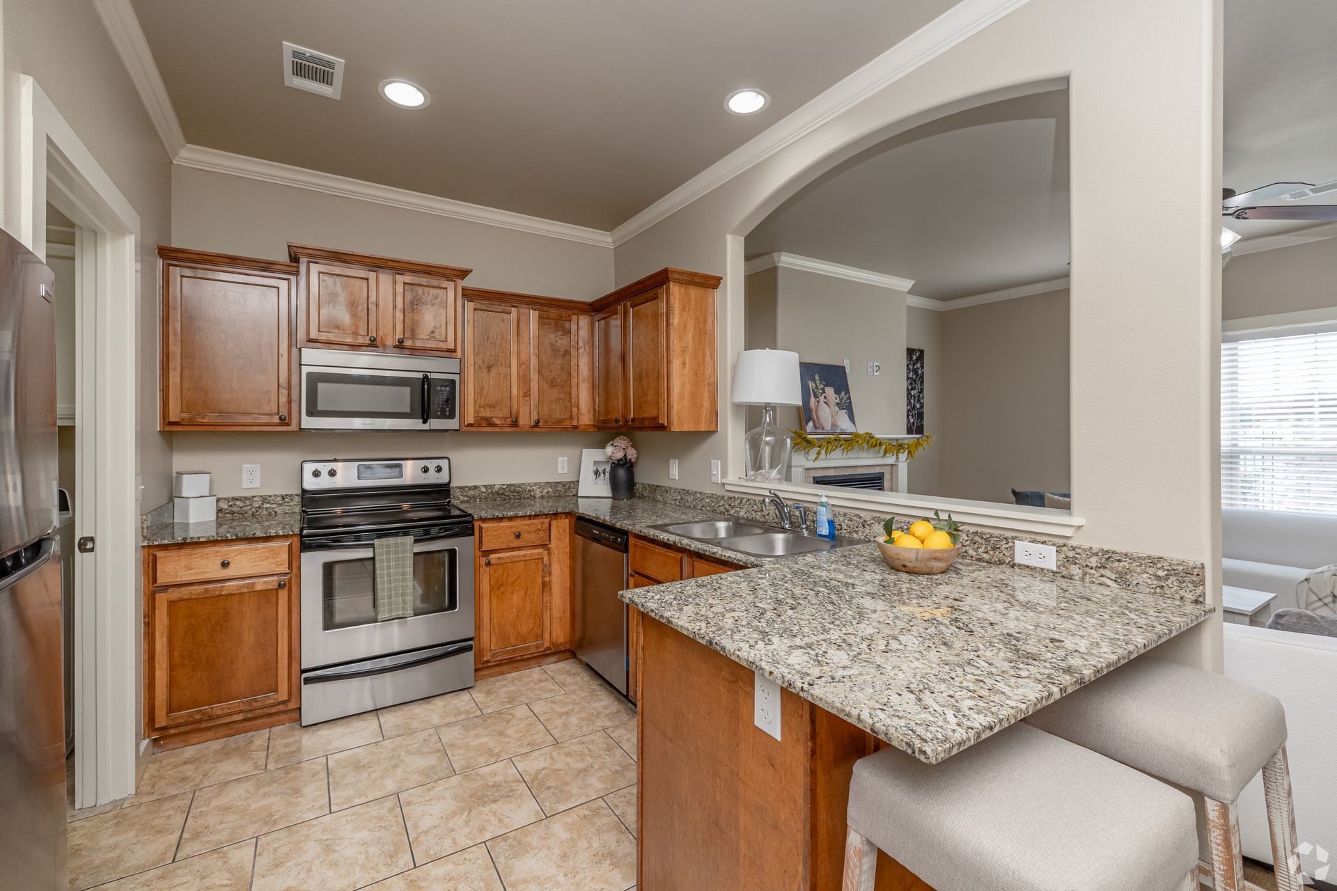Kitchen with stainless steel appliances, granite countertops, and wooden cabinets.  Bar seating and an archway.
