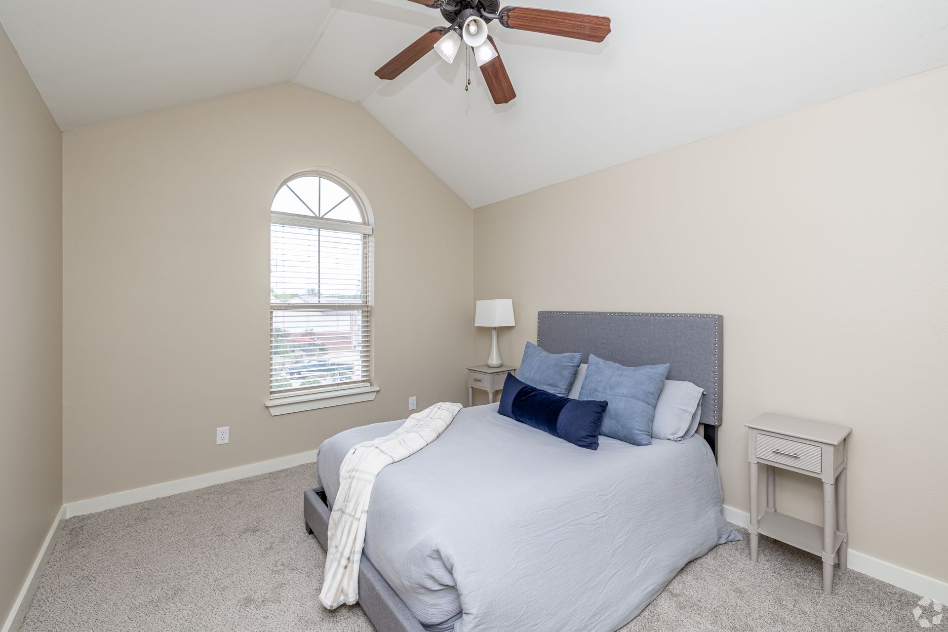 Bedroom with bed, nightstand, arched window, ceiling fan, and gray carpet.