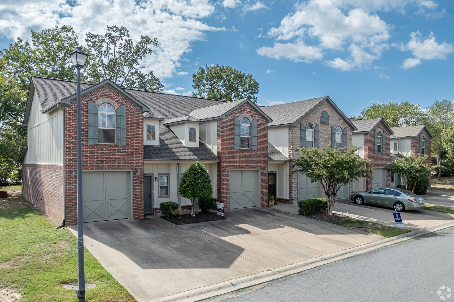 Townhouses with brick and stone facades, garages, and driveways on a sunny day.