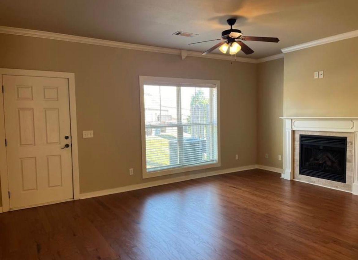 An empty living room with hardwood floors , a fireplace and a ceiling fan.