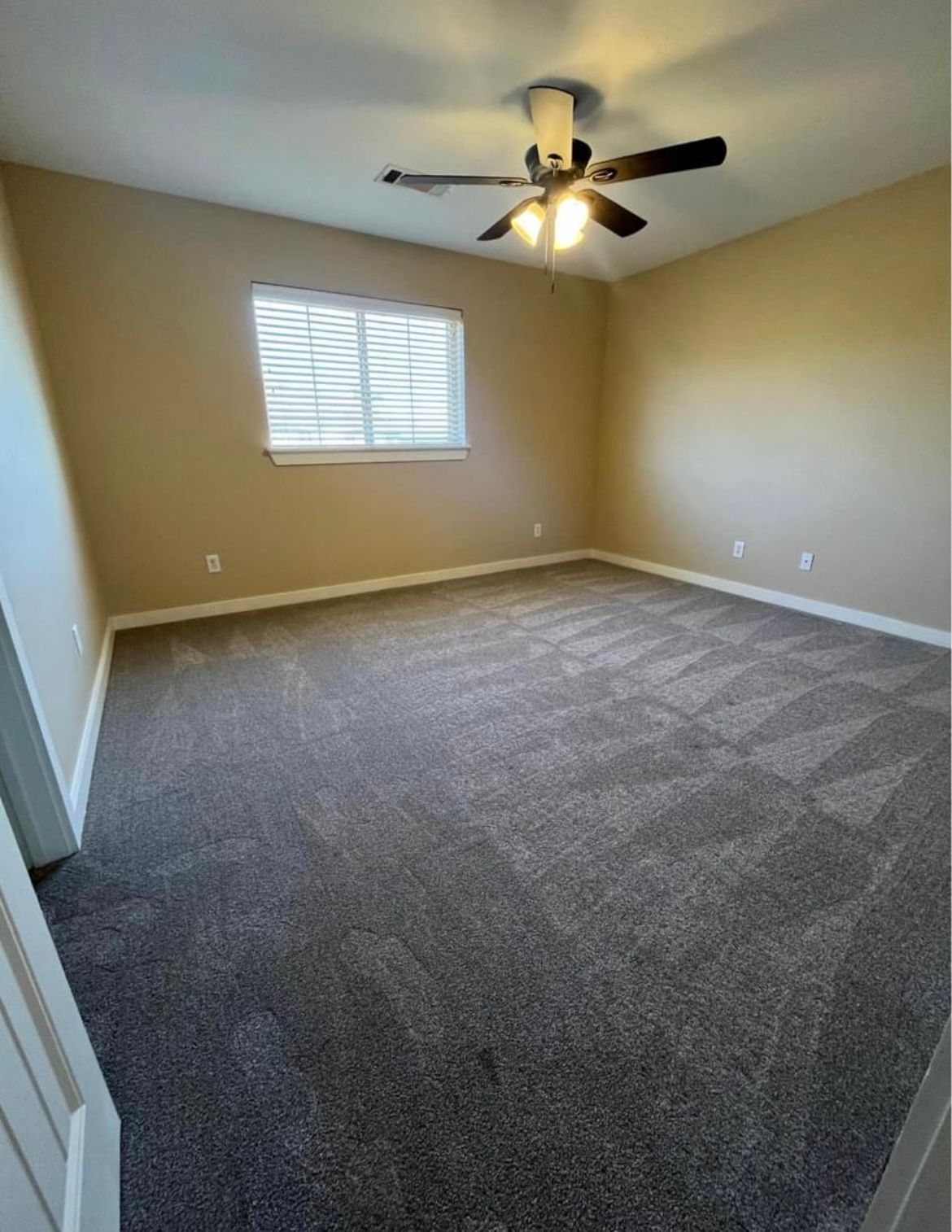 An empty bedroom with a ceiling fan and a window.