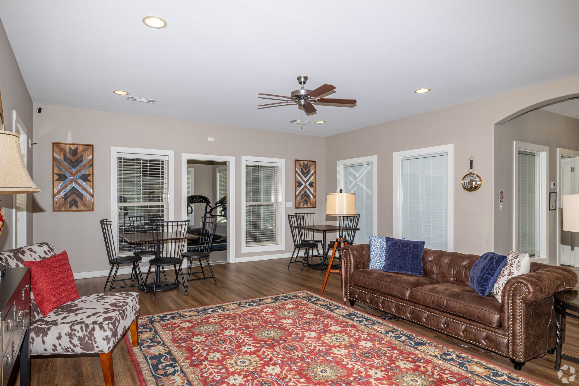 Spacious living room with brown leather sofa, patterned rug, tables, chairs, and large windows.