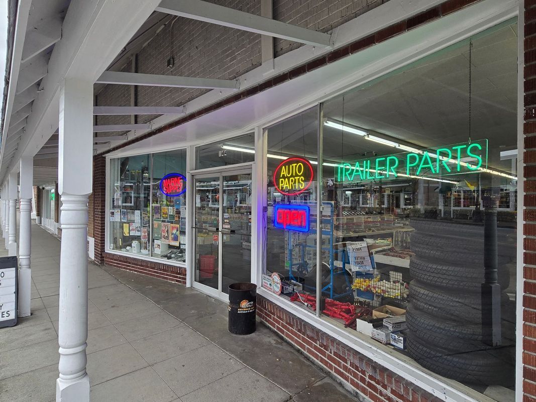Trailer parts store with large windows and neon signs; tires stacked inside.