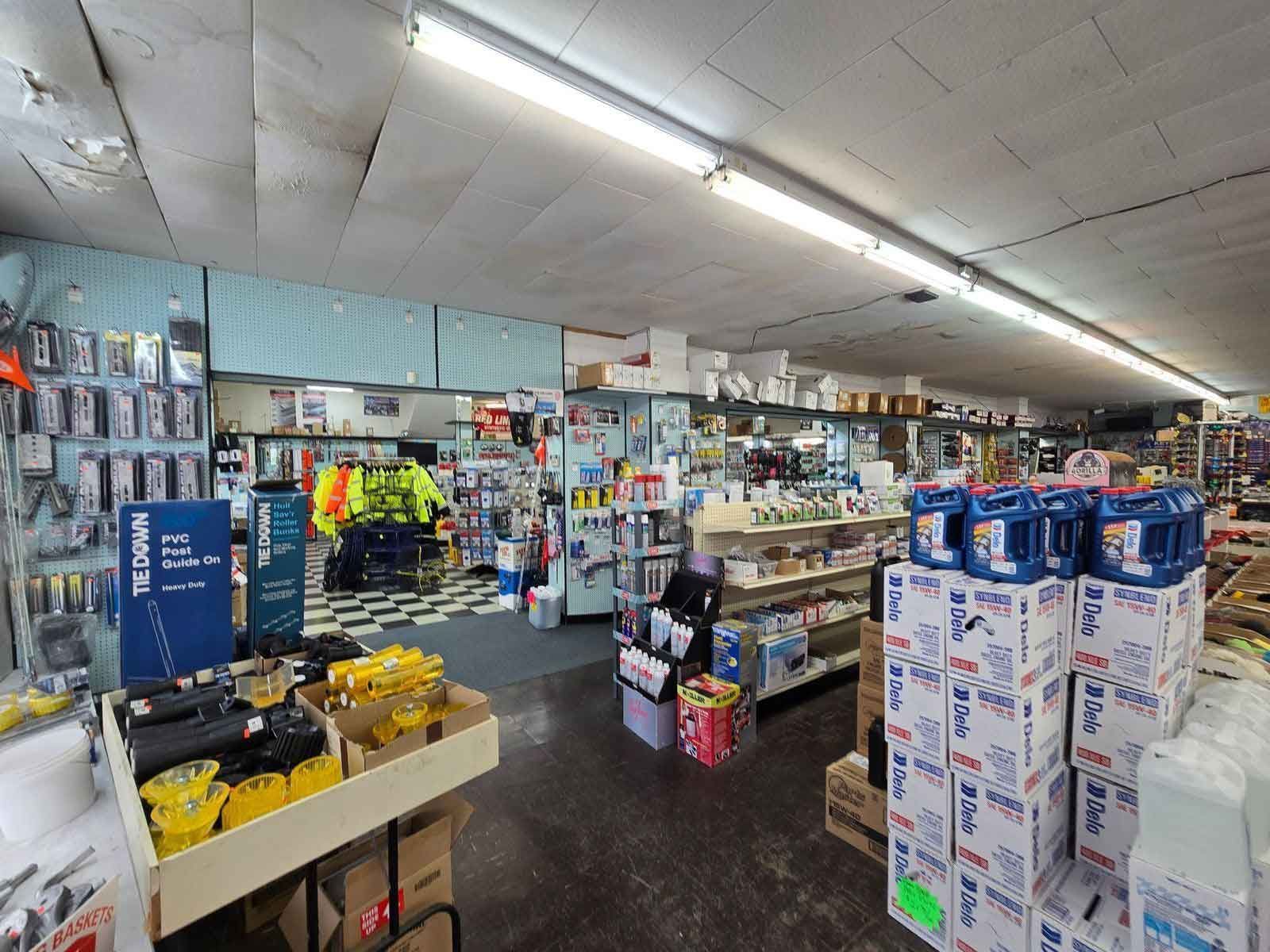 Interior view of a hardware store with various merchandise on shelves and displays under fluorescent lights.