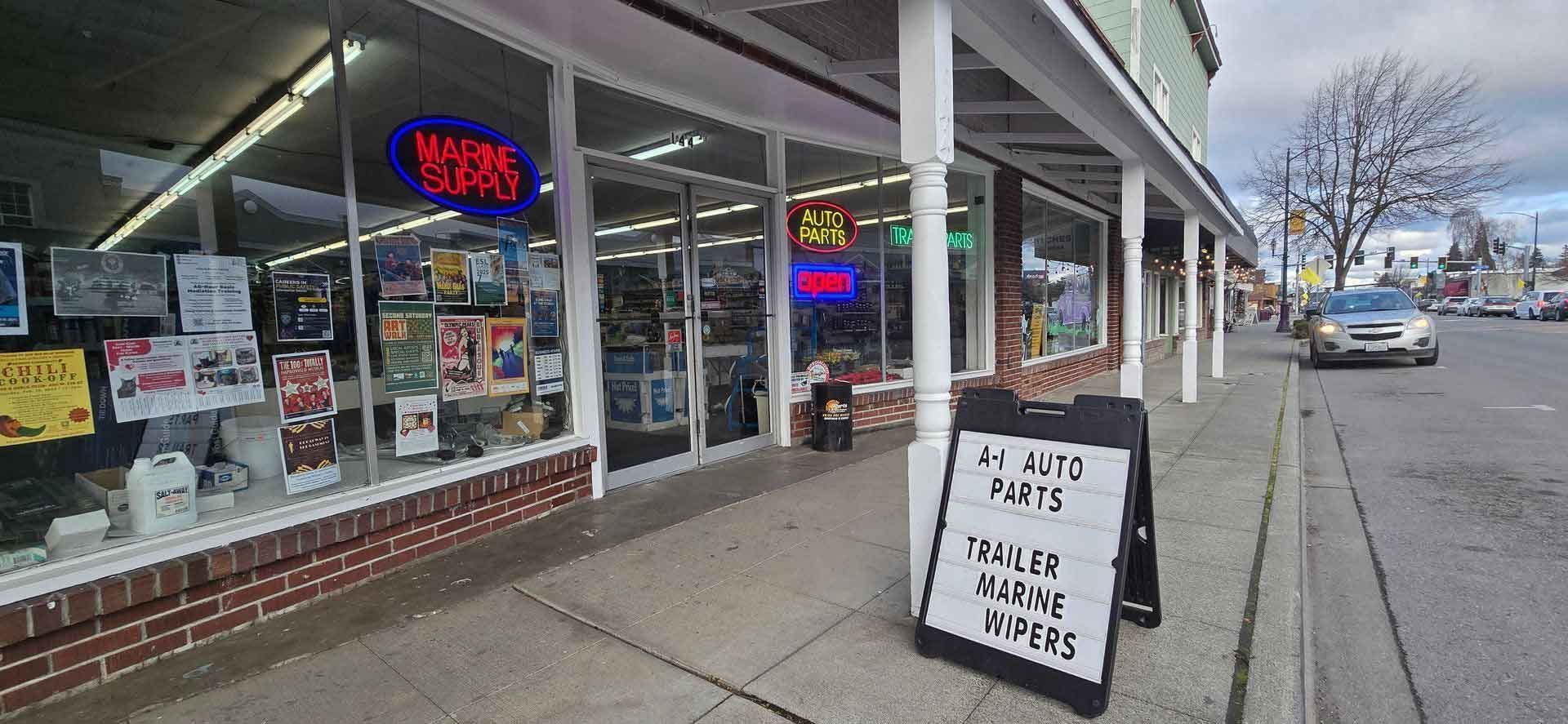 A shop with a neon sign and an A-frame sign on a sidewalk. A car drives by on a street.