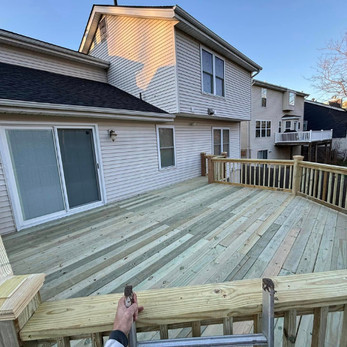 New wooden deck attached to a two-story house. Man's hand holds a tool on the railing.