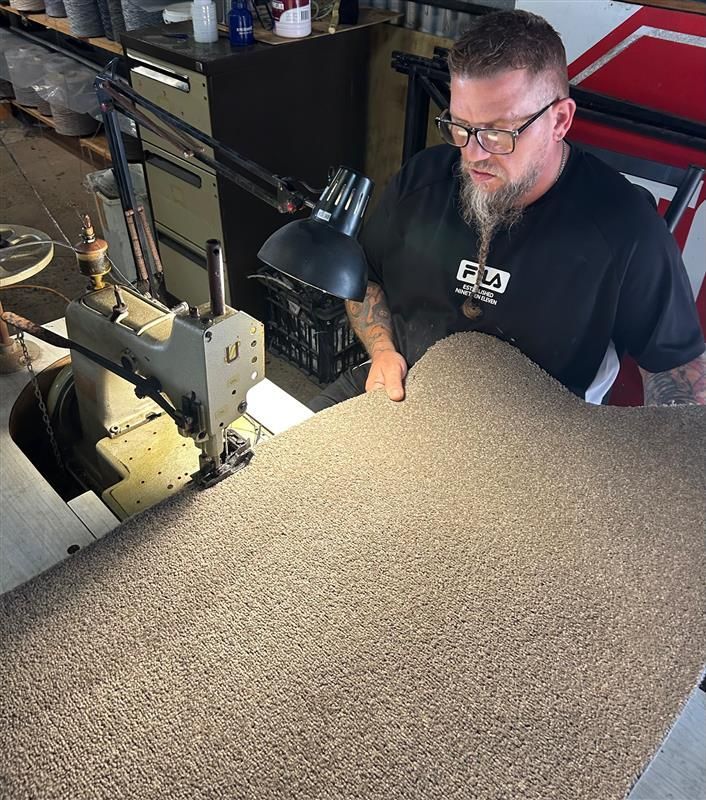 Man using sewing machine to edge large carpet — Carpet Edging - Bundaberg Carpets and Vinyls