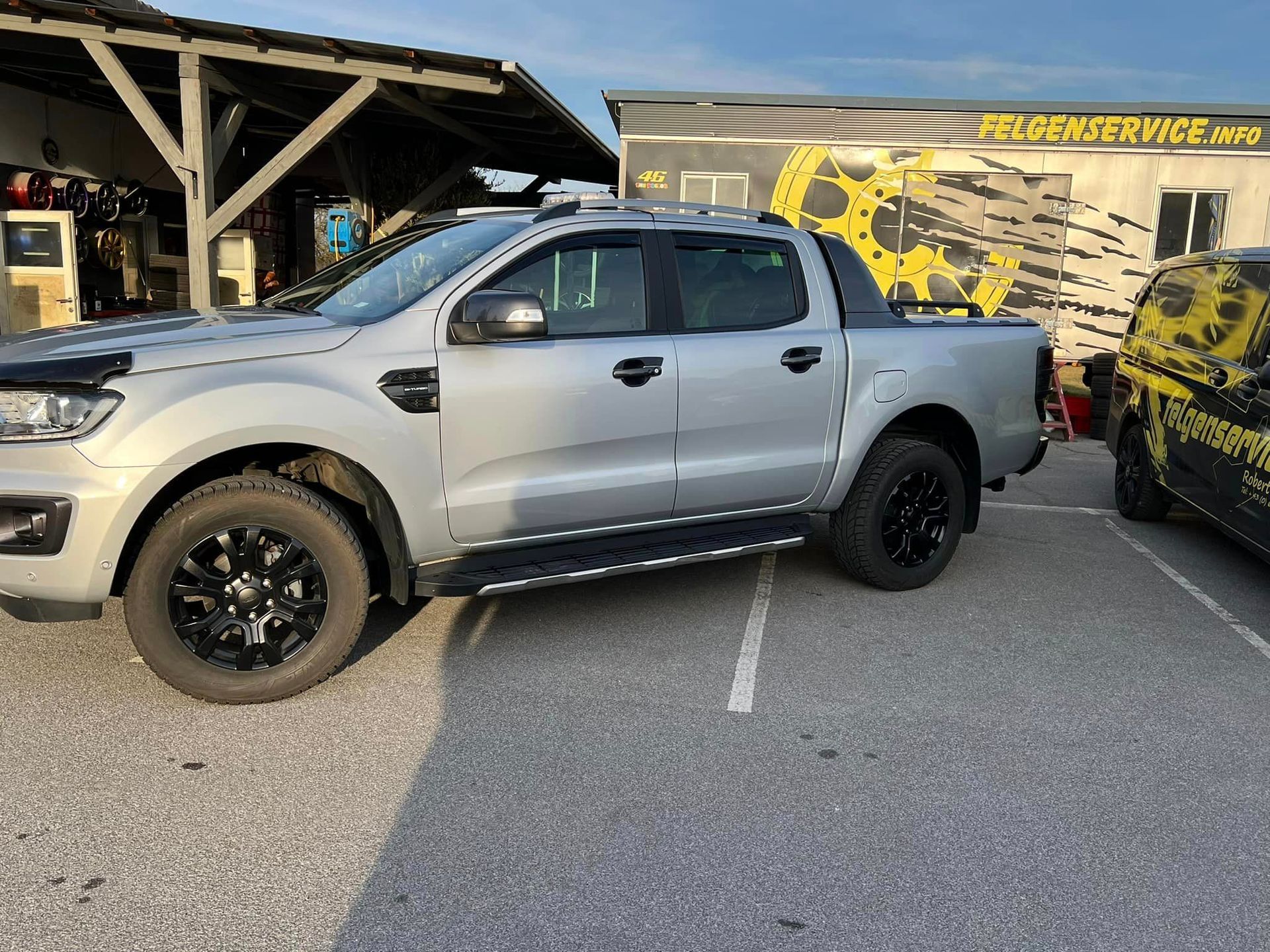 ein silberner Pickup-Truck steht vor einem Felgenservice-Geschäft