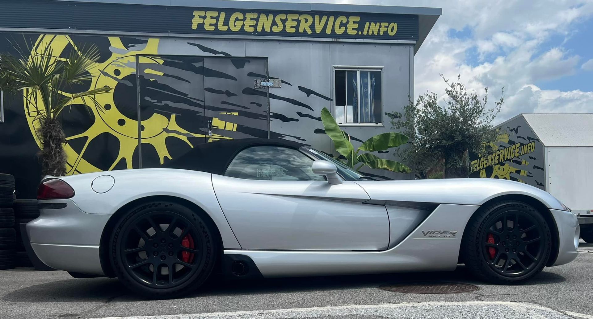 Vor einem Gebäude mit der Aufschrift „felgenservice.info“ parkt ein silberner Sportwagen