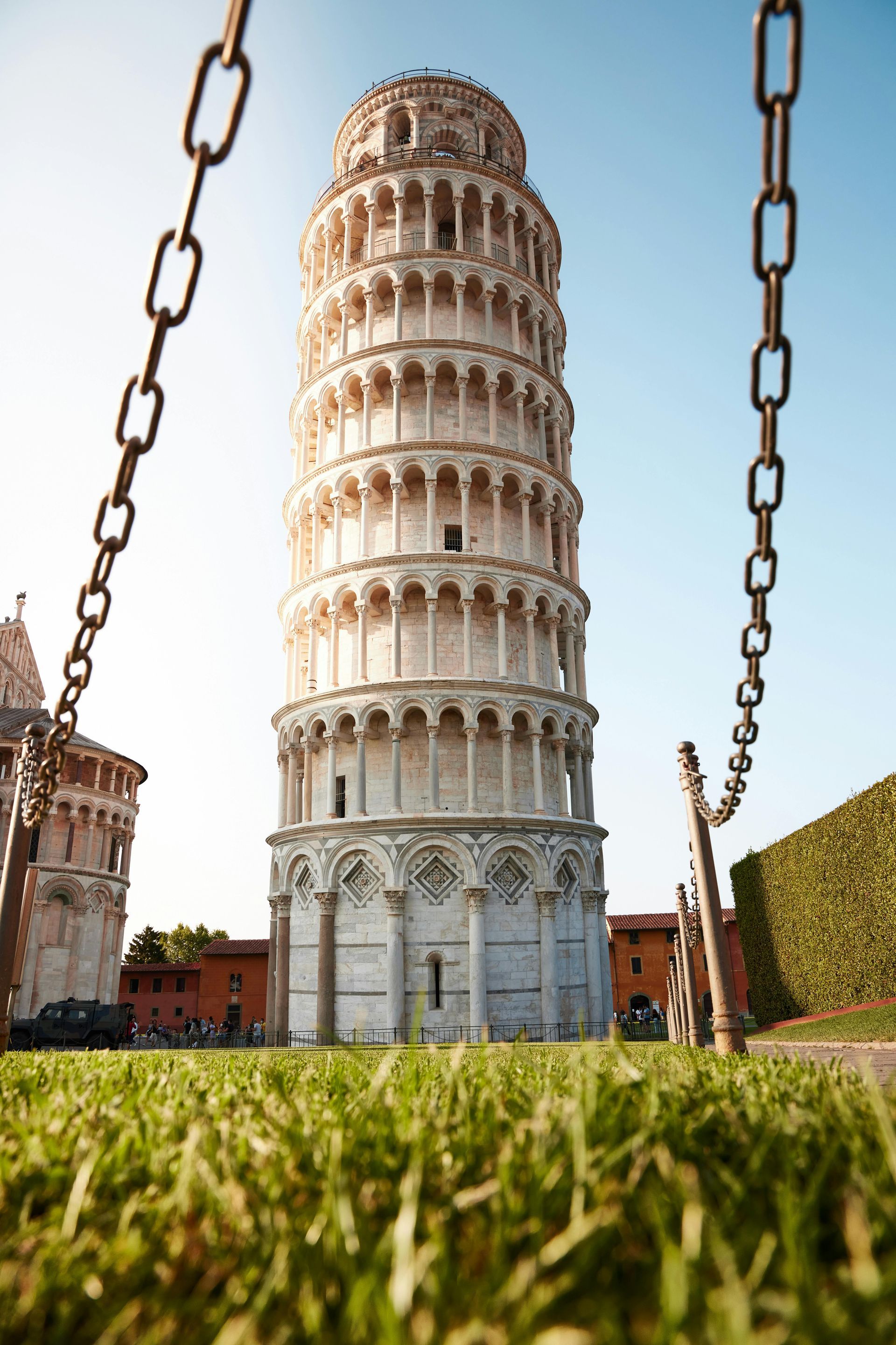 La torre pendente di pisa è circondata da catene nell'erba.