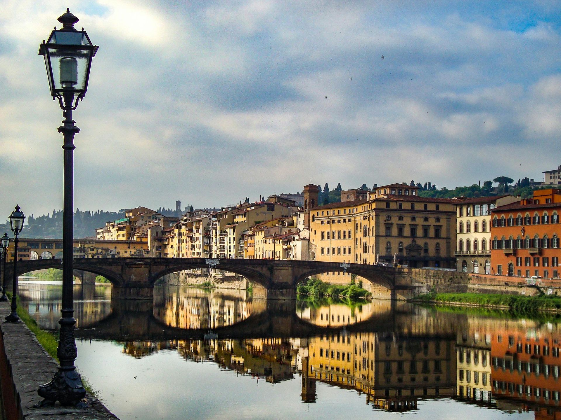 Un ponte e degli edifici si riflettono nel fiume calmo di Firenze, in Italia, sotto un cielo nuvoloso.