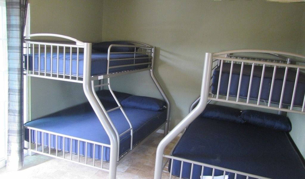 A bedroom with a window , chair , trash can and air conditioner.