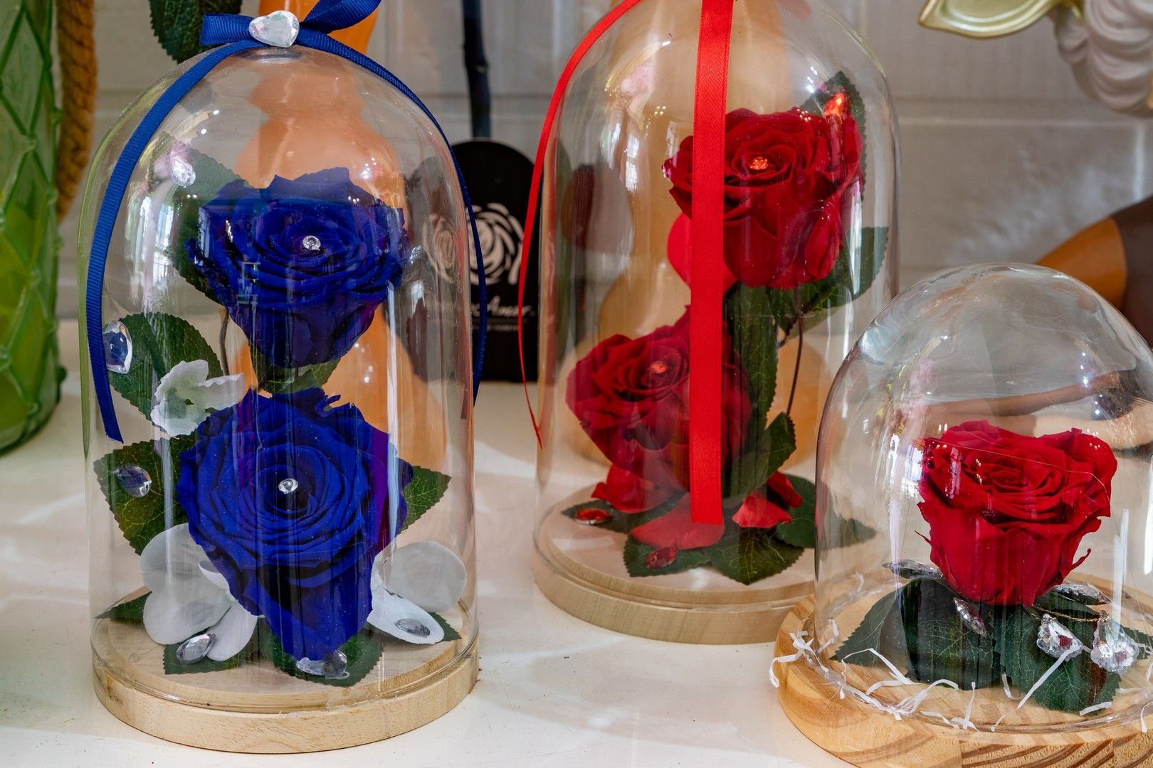 Tre campane di vetro riempite con rose rosse e blu sono appoggiate su un tavolo.