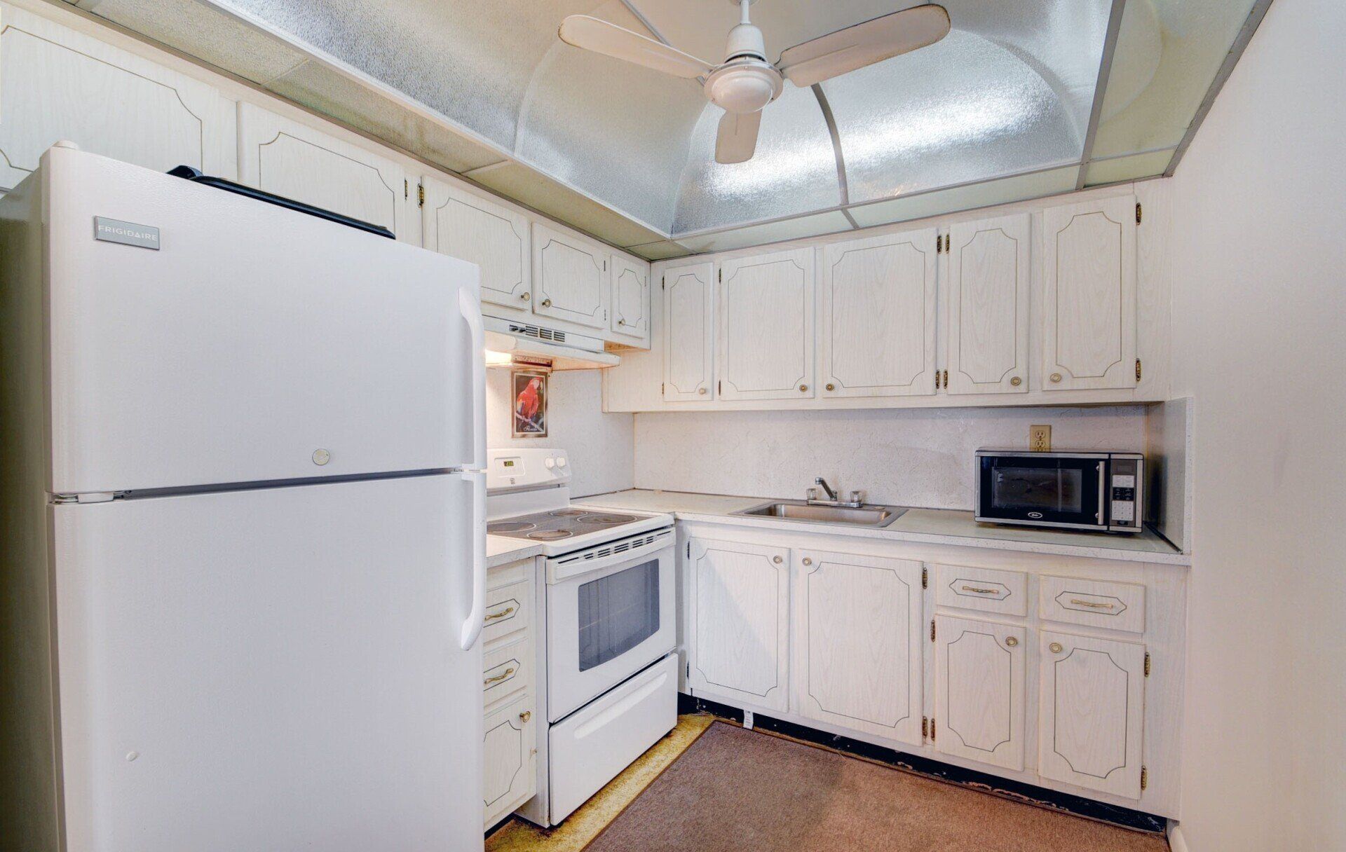 A kitchen with white cabinets , a refrigerator , stove , microwave and ceiling fan.