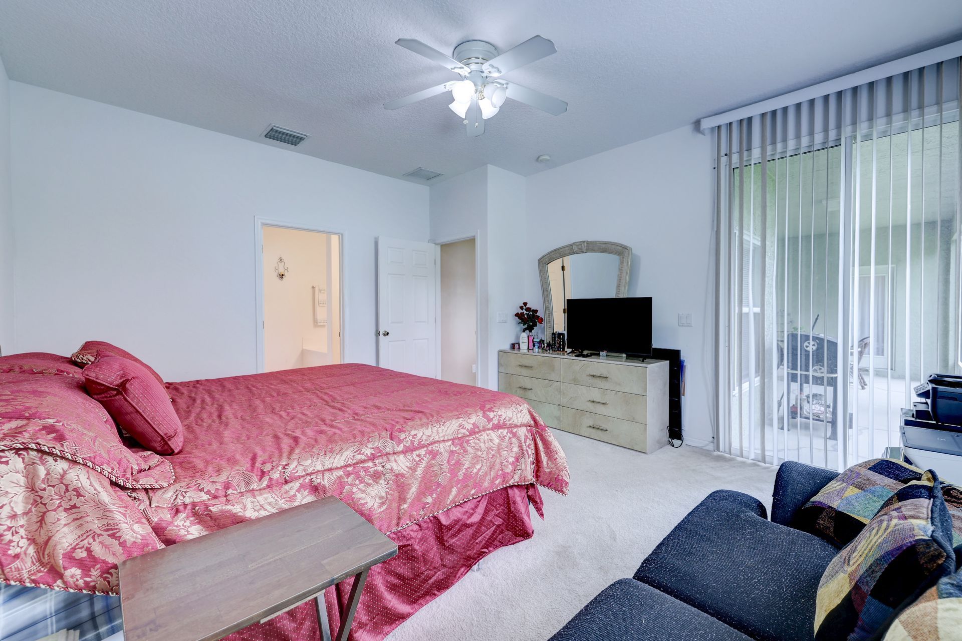 A bedroom with a large bed , a couch , a television and a ceiling fan.