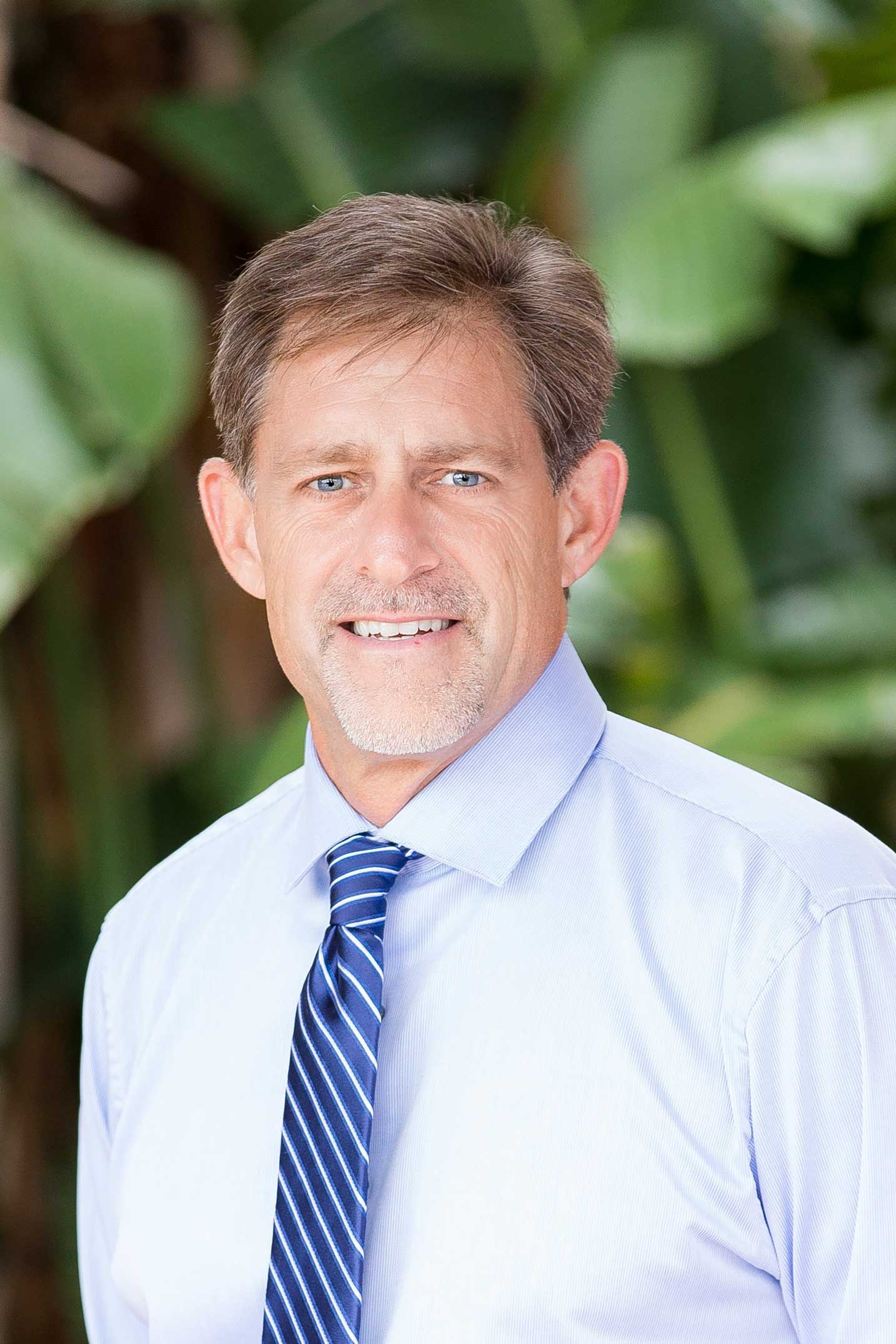 A man in a white shirt and blue tie is smiling for the camera.