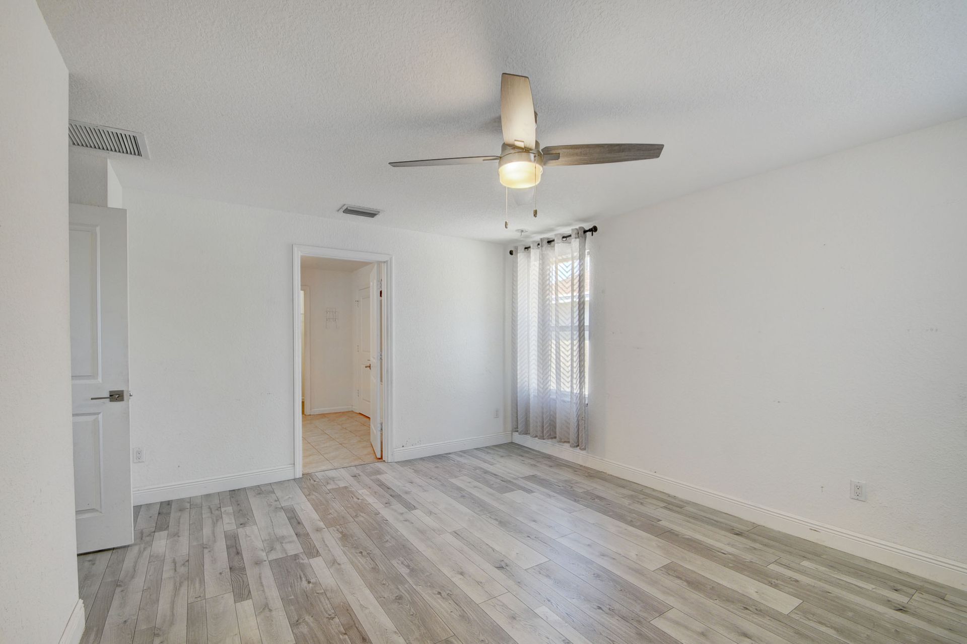 An empty living room with hardwood floors and a ceiling fan.