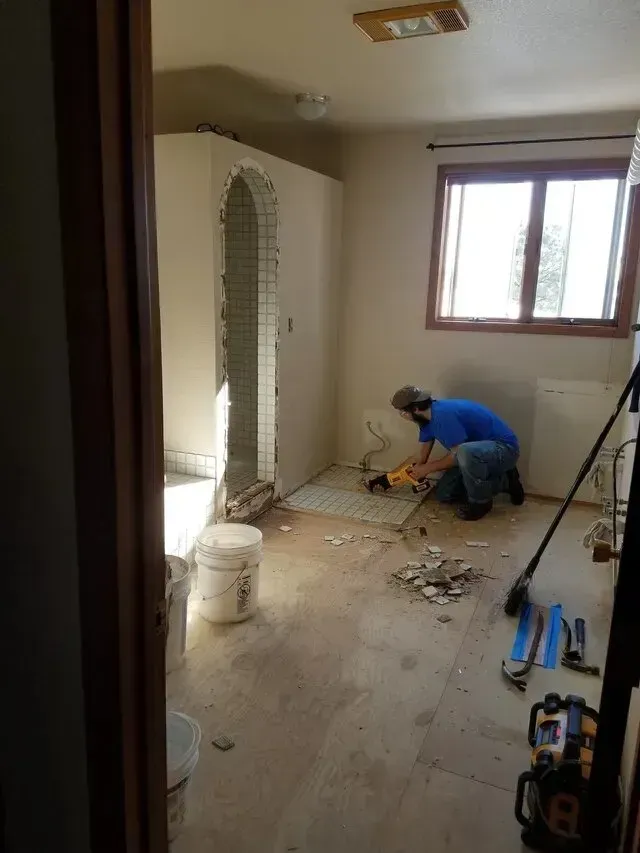 A man is working on a tile floor in a bathroom.