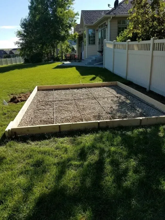 A backyard with a fence and a gravel area in front of a house