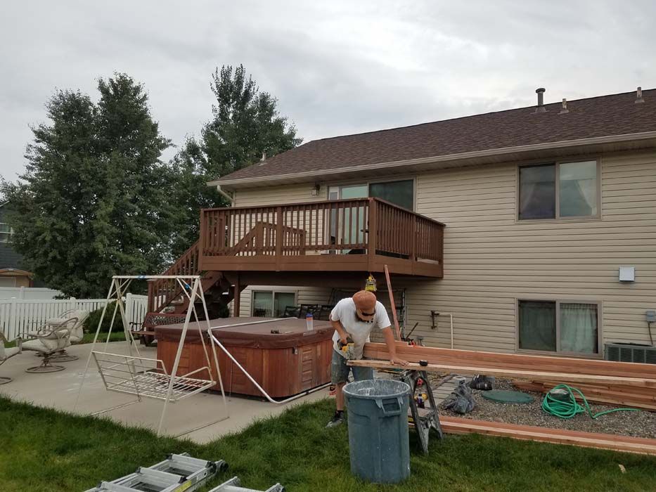 A man is working on a wooden deck in front of a house.