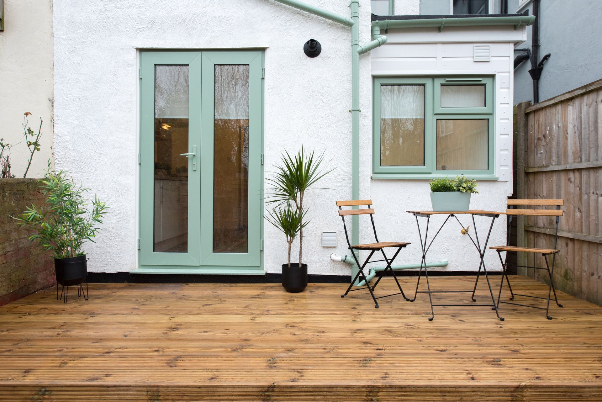 A wooden deck with a table and chairs in front of a house.