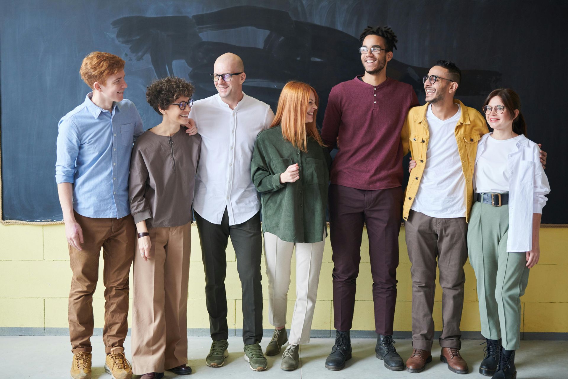 Group of eight people smiling, posing together in front of a chalkboard.