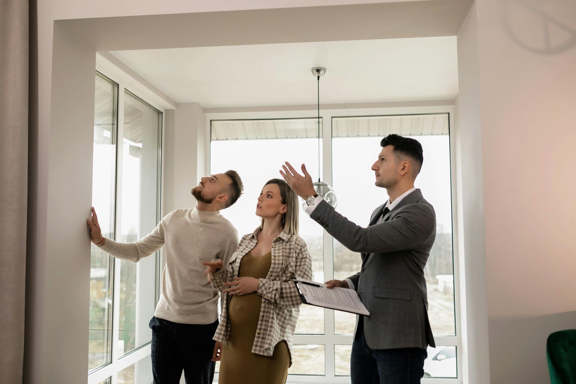 Real estate agent showing a couple a room with large windows, gesturing toward the view.