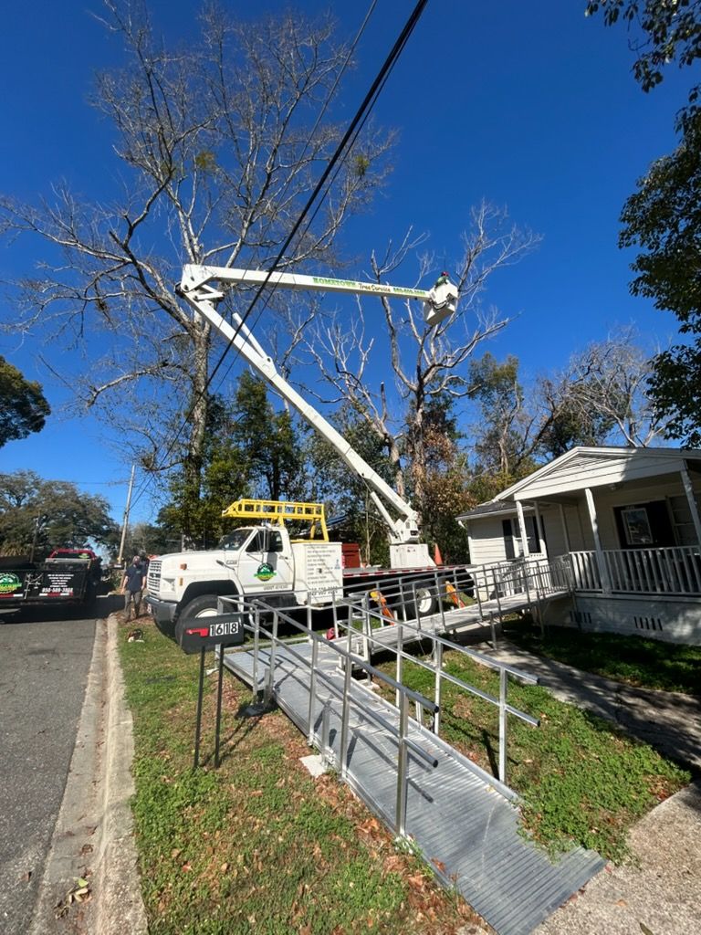 A white utility truck with an extended boom lift parked next to a house with a metal wheelchair ramp in a suburban yard.