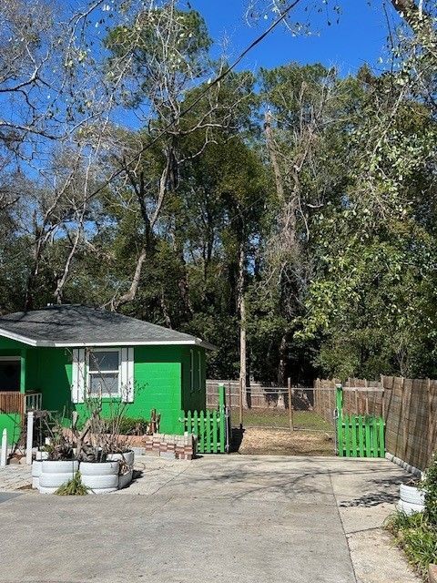 A bright green house with a small front yard, a white planter, and a green wooden gate opening to a wooded area.