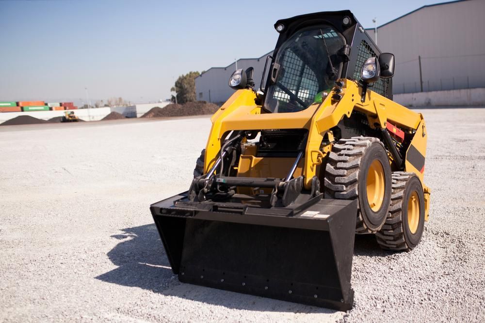 A Yellow Tractor With a Black Bucket is Parked in a Gravel Lot — Hothams In Lithgow, NSW