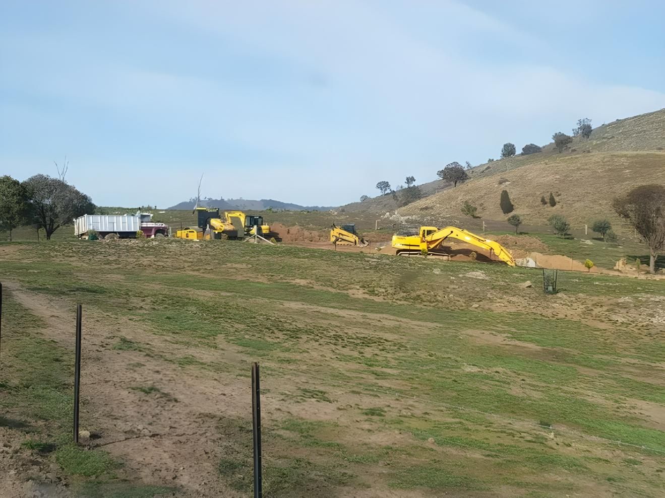 A Large Yellow Excavator is Sitting in the Middle of a Grassy Field — Hothams In Bathurst, NSW