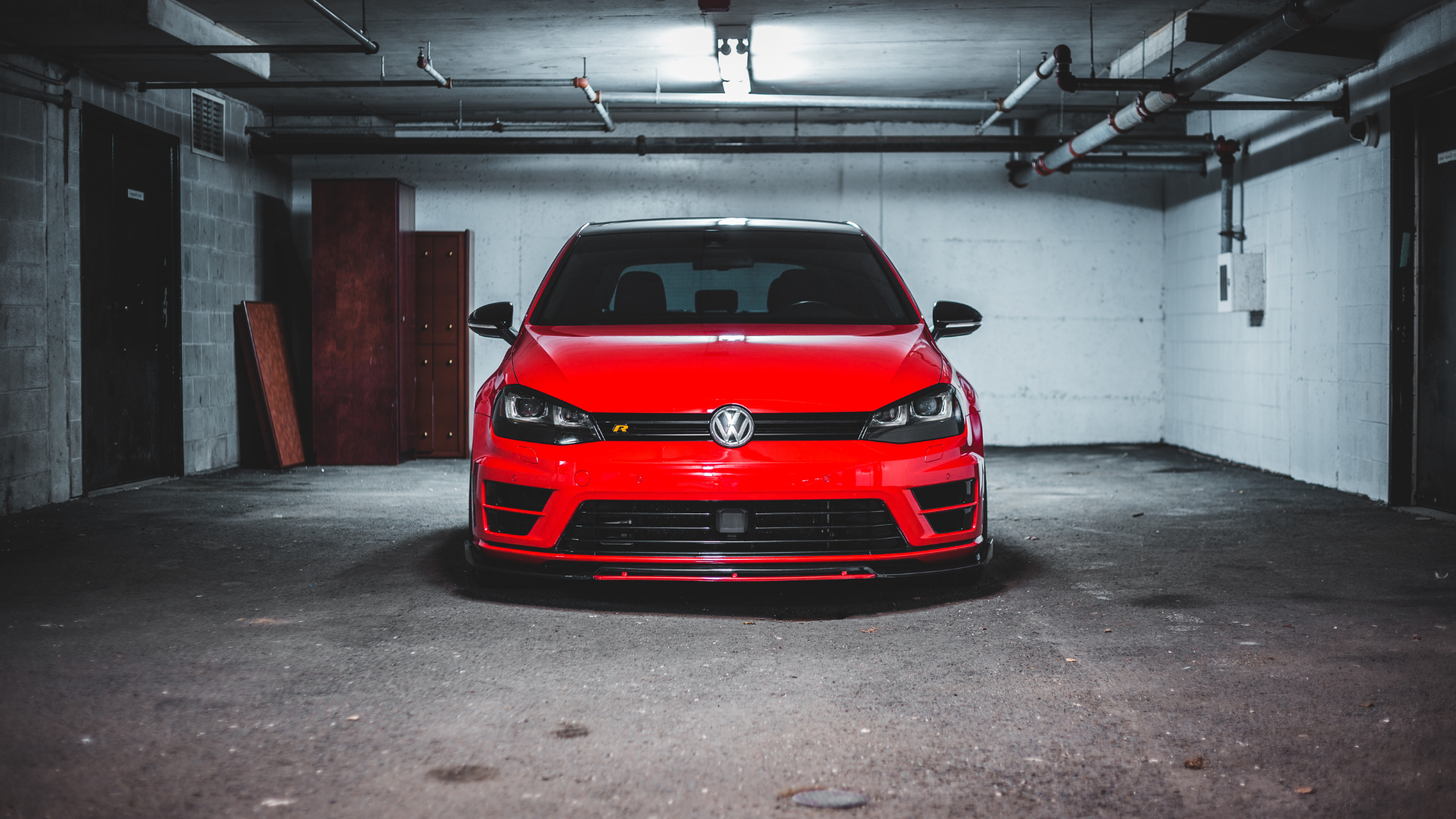 Red Volkswagen Golf R parked in a dim garage, illuminated by overhead lights.