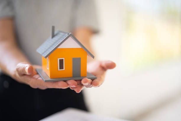 Person holding a small orange house model in their hands, suggesting home ownership or real estate.