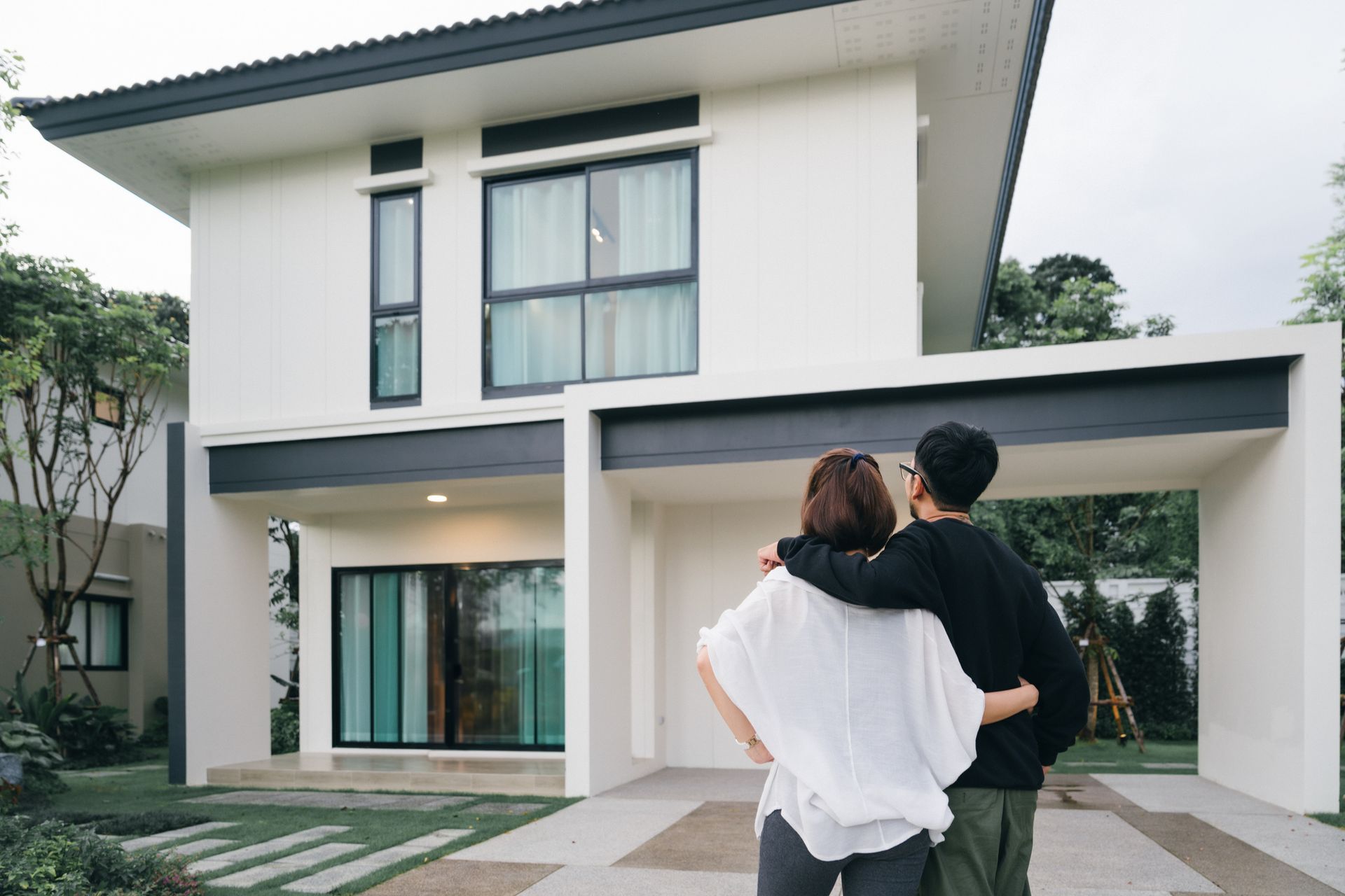 A happy couple looking at their white, big house, showcasing homeowner's insurance.