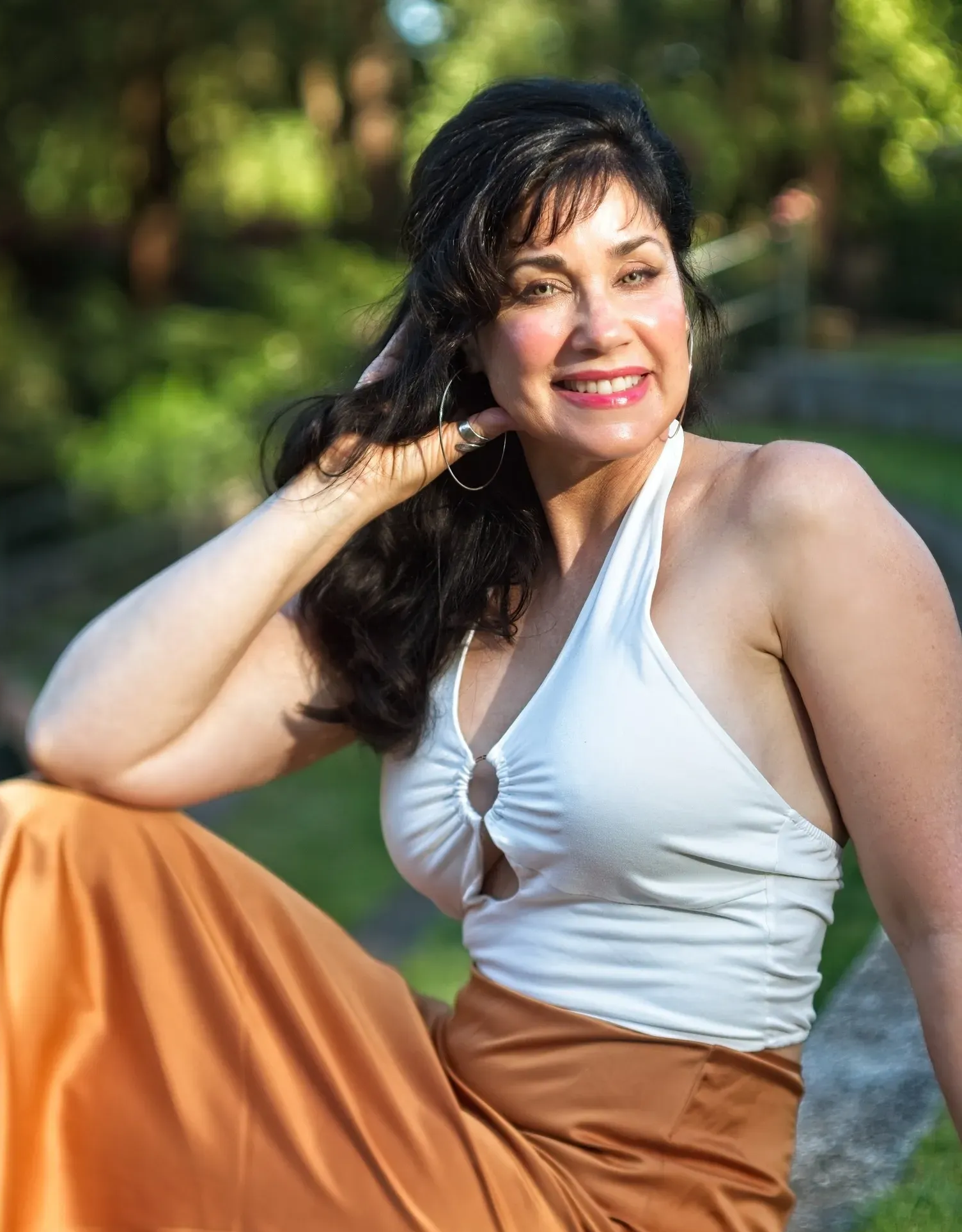 Patricia in white halter top and orange skirt smiling outdoors, hand in hair.