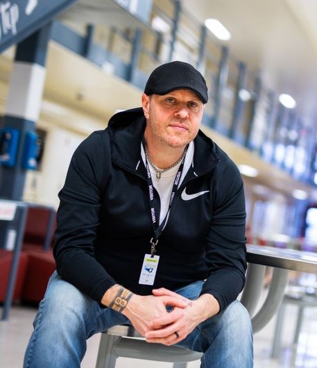 A man wearing a nike jacket is sitting on a stool