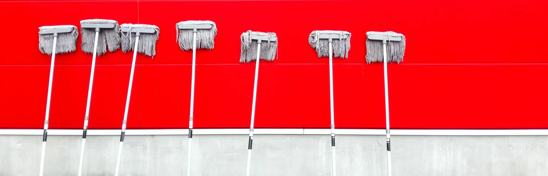 A row of mops against a red wall.