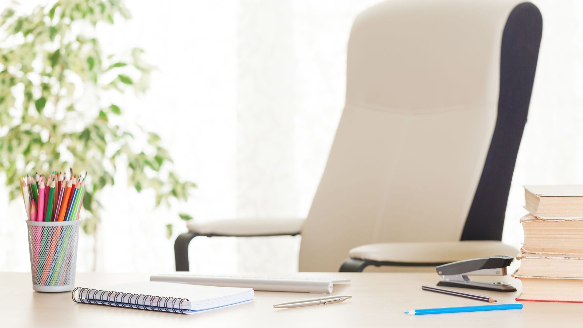 A desk with a chair , books , pencils and a laptop on it.