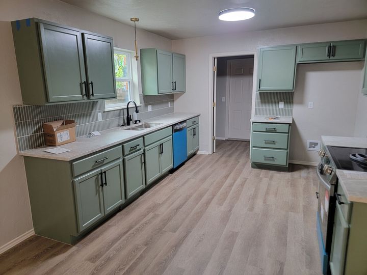 A kitchen with sage green cabinets, light countertops, patterned backsplash, and wood-look flooring.