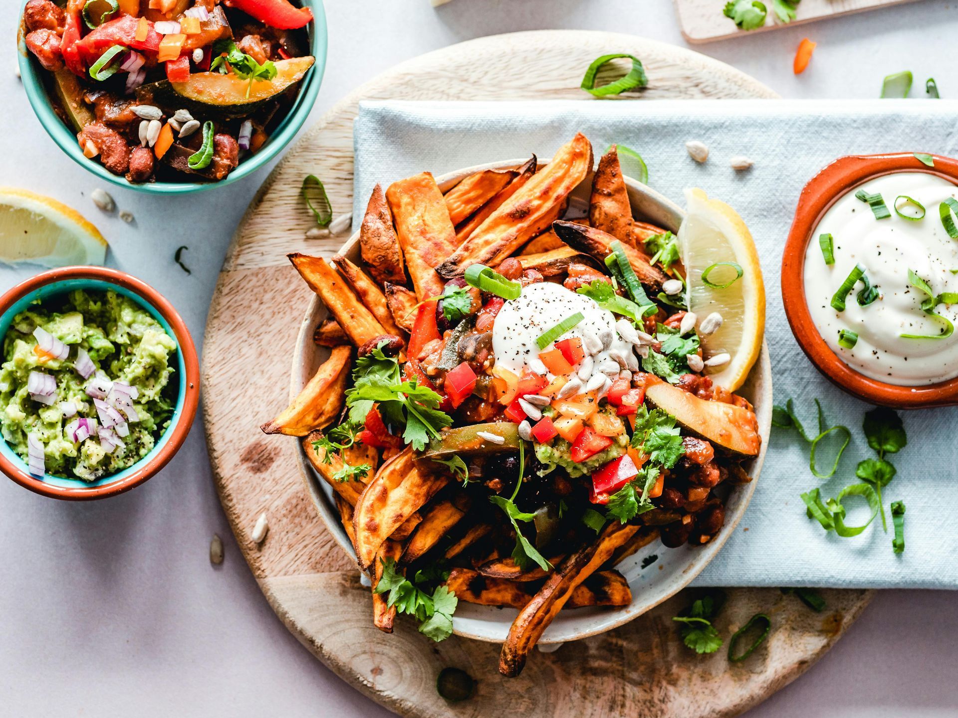 A bowl of sweet potato fries topped with beans, salsa, and sour cream, served with guacamole and a side of yogurt dip.