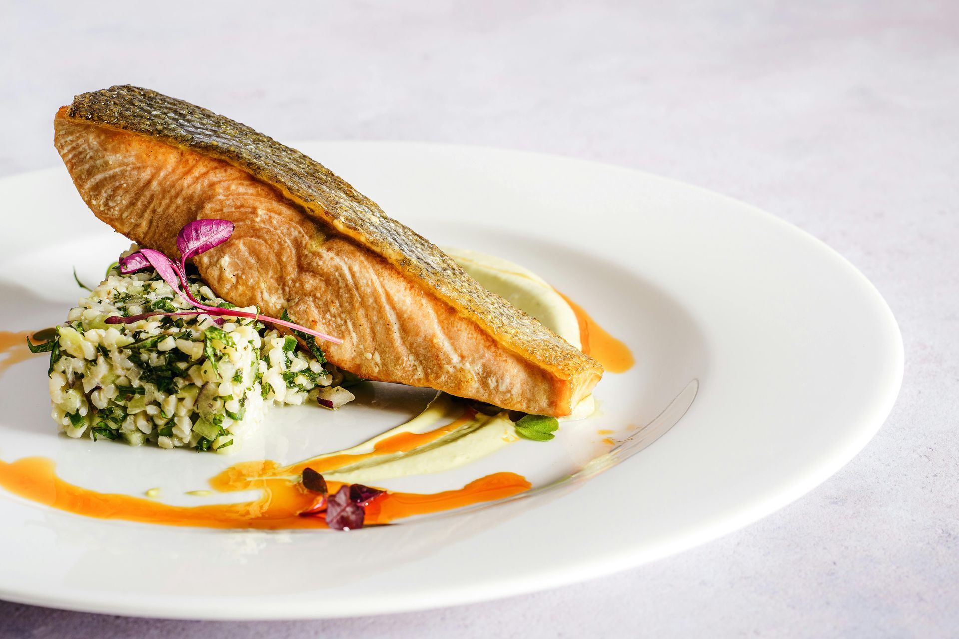 A pan-seared salmon fillet served on a bed of green herb rice with a vegetable purée and drizzle of orange oil.
