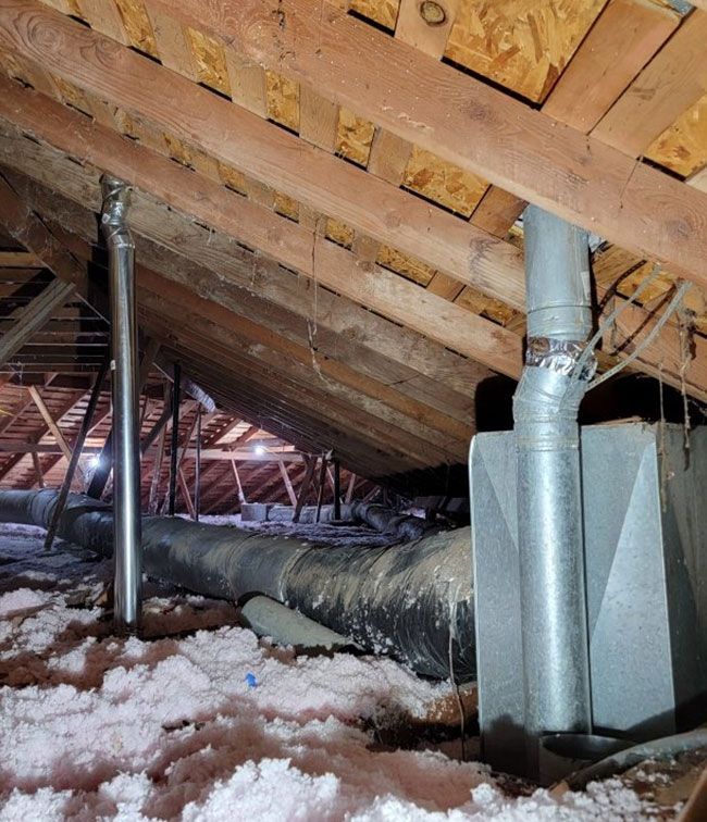 Attic with exposed rafters, insulation, HVAC ducts, and a snowy leak stain on the floorboard surface
