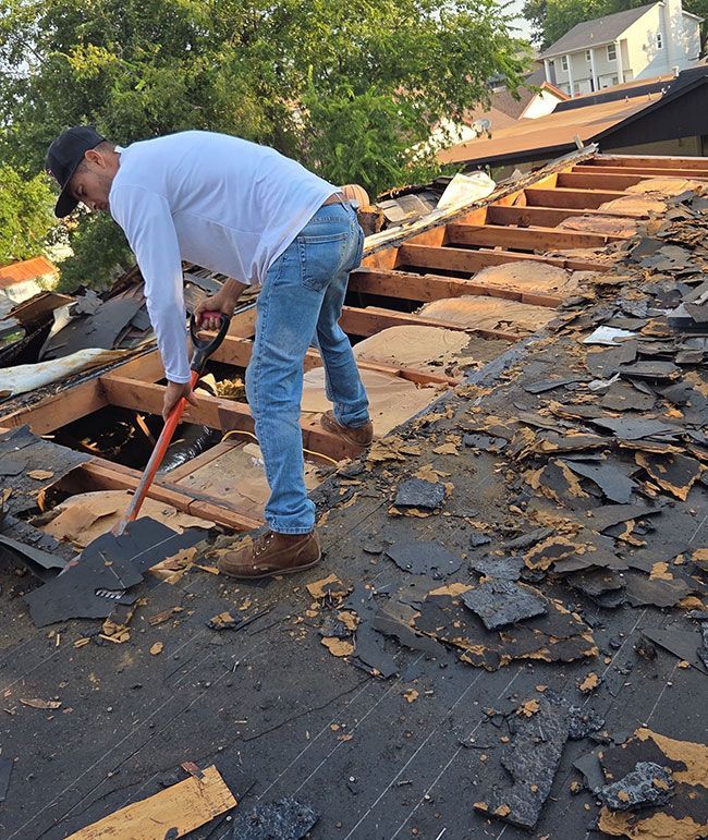 Worker removing shingles from a damaged roof with a pry bar during roof repair.