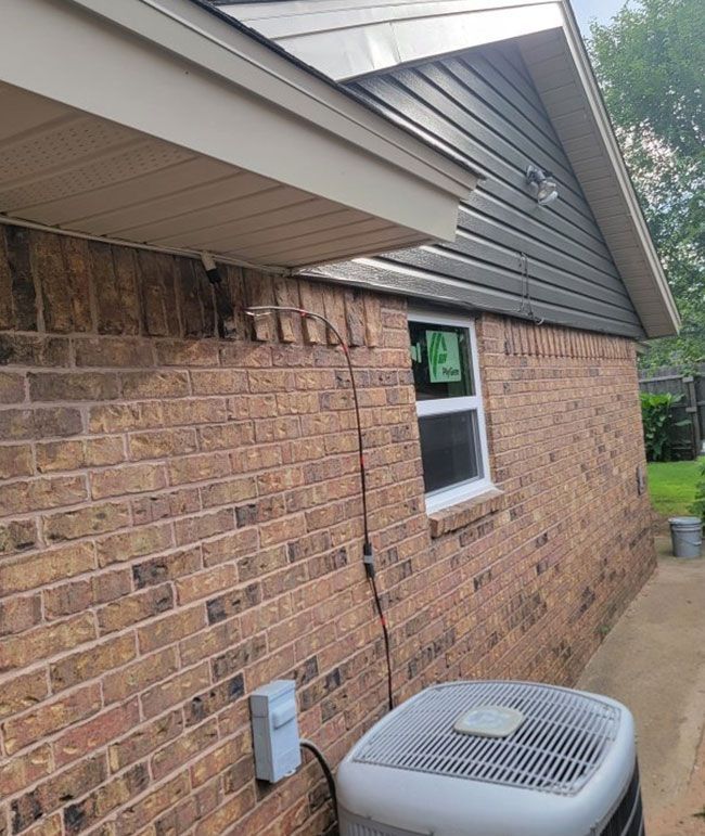 Brick house exterior with soffit damage and a window air conditioner below the eaves