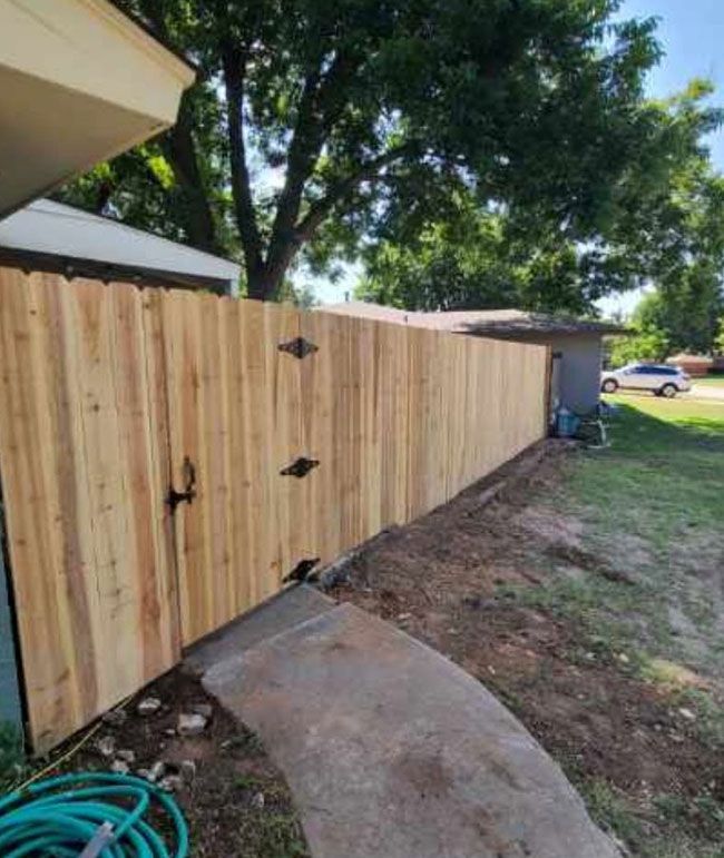 Wooden privacy fence with black hinges beside a curved concrete walkway in a grassy yard.