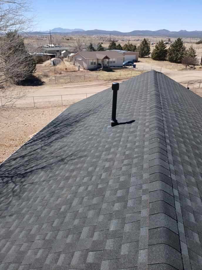 Rooftop shingles with a black vent pipe overlooking a desert neighborhood and mountains
