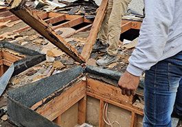 Damaged roof with debris and broken beams after storm, with a person inspecting the damage